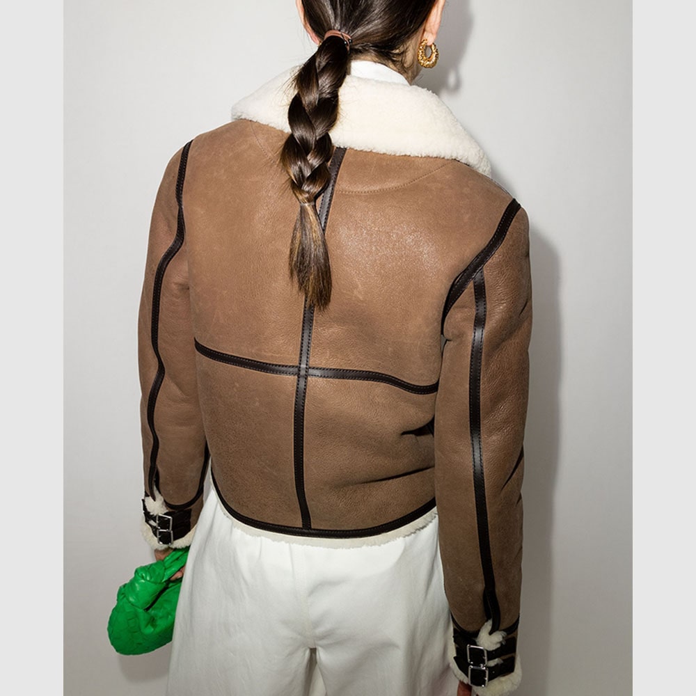 A brown LOEWE shearling aviator jacket with a cream-colored shearling collar, double straps, a zipped front closure, a contrast leather patch front pocket, a zipped front pocket, and contrast leather piping.