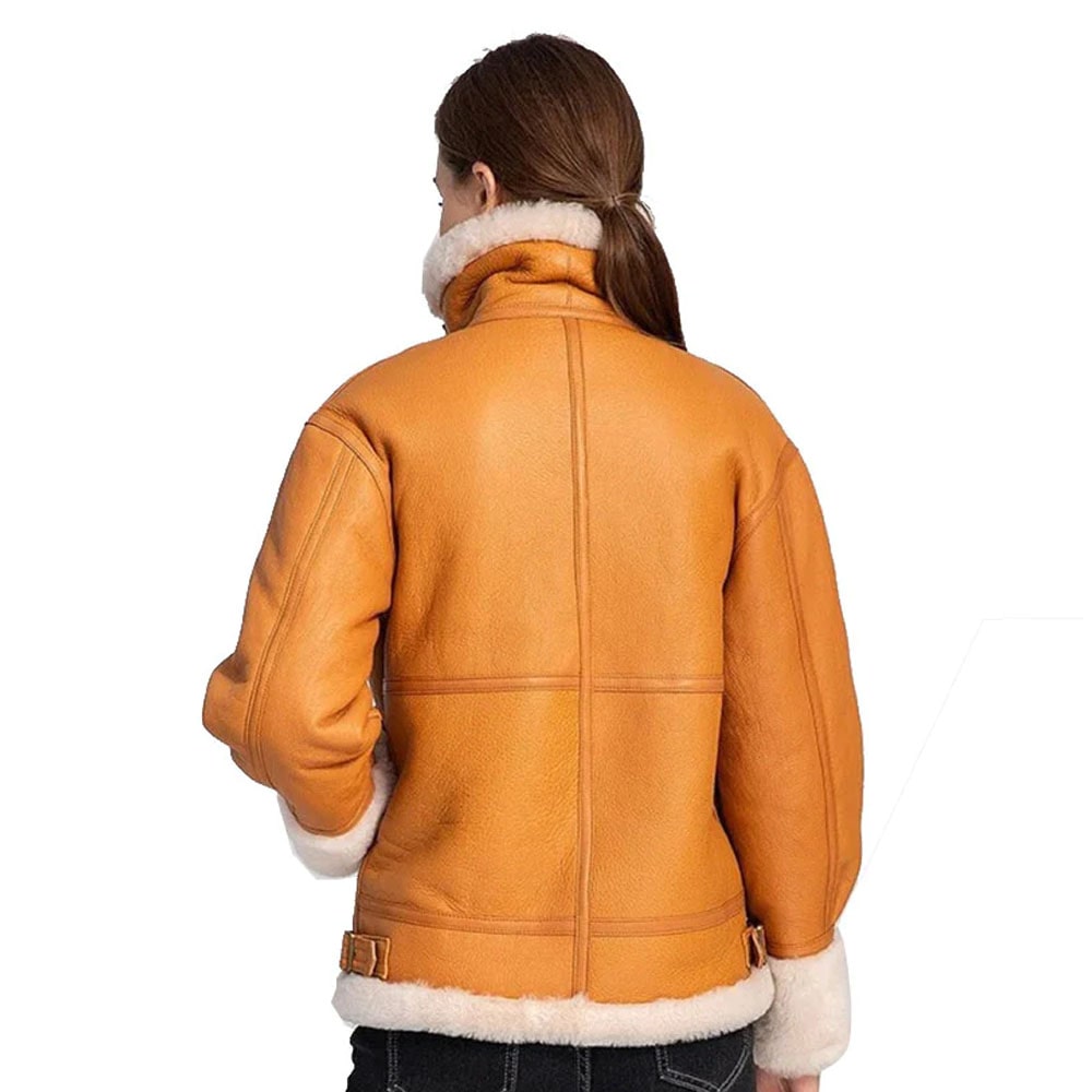 A woman wearing a brown shearling leather bomber jacket with white collar and cuff details, paired with black pants.
