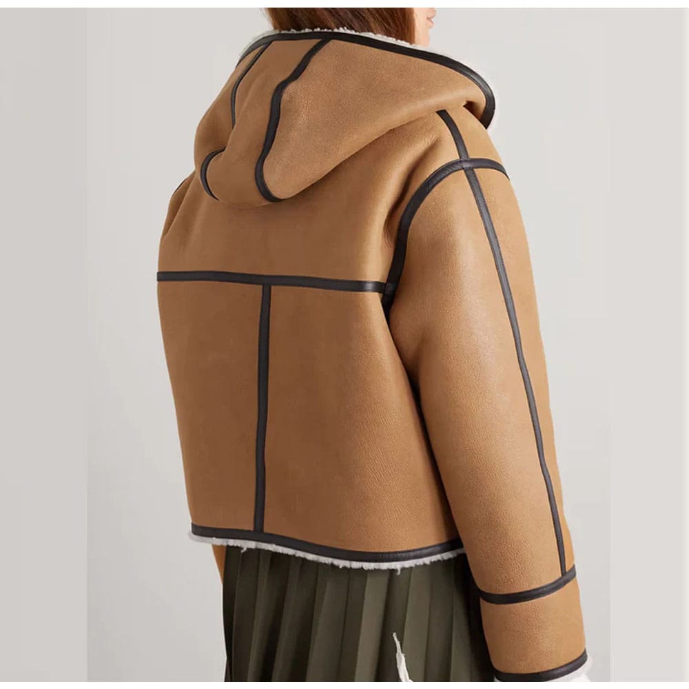 A hooded leather-trimmed sheepskin shearling bomber leather jacket in tan color with a zipper and button details, displayed on a white background.