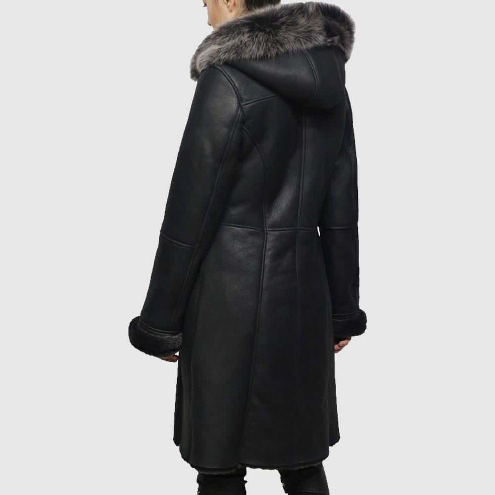 A black, double-breasted, shearling sheepskin jacket with a hood, featuring a soft suede exterior and Toscana sheepskin interior. It has buttoned closures and vertical pockets on the sides.