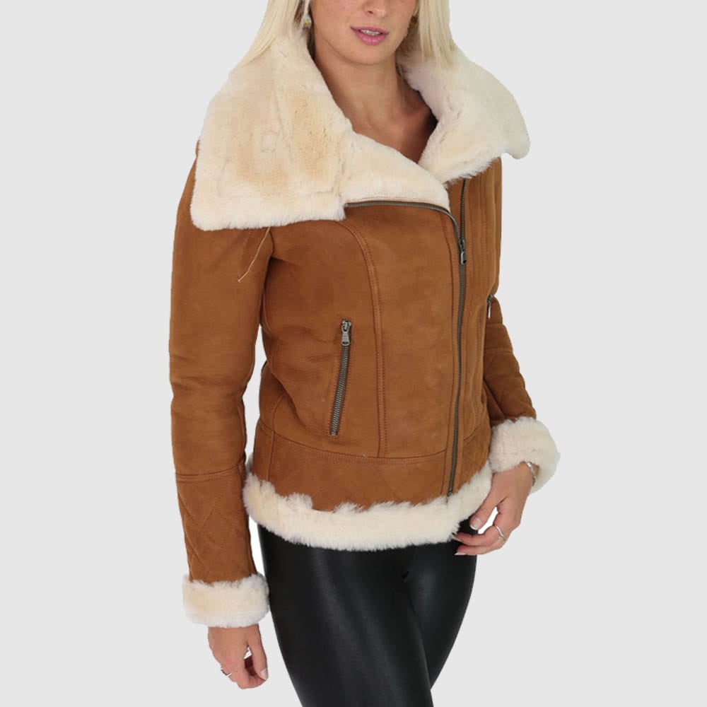 A woman wearing a tan shearling leather jacket with a stand-up collar and fur lining, paired with black pants.