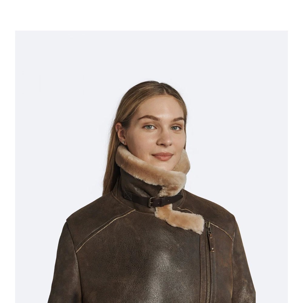 A woman standing outdoors wearing an oversized brown shearling leather jacket with a fur collar, belt, and zipper details.